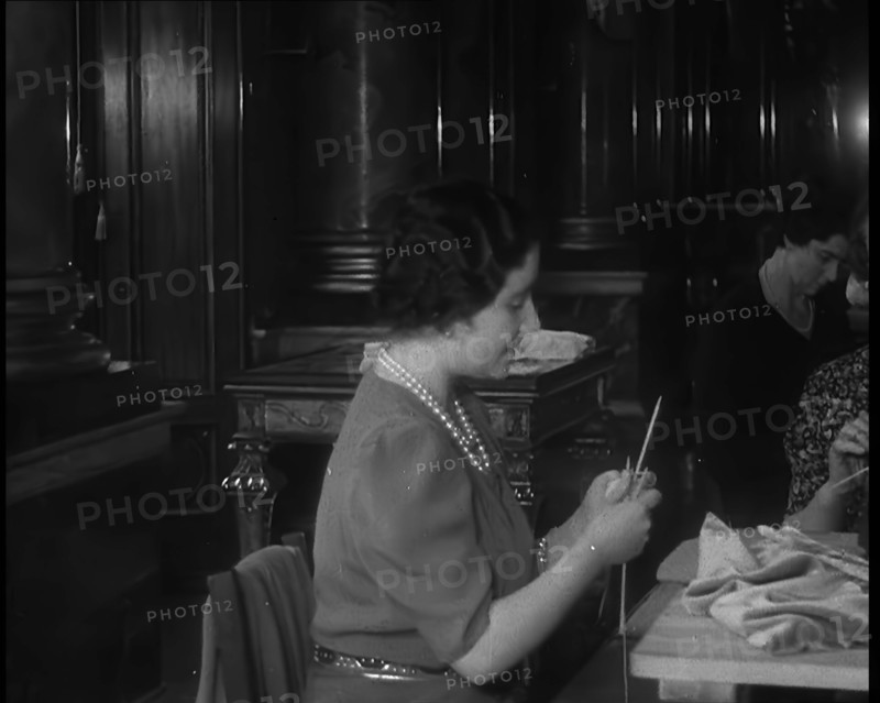 Queen Elizabeth Knitting at a Large Sewing Group Hosted in Buckingham Palace, 1940. Creator: British Pathe Ltd.