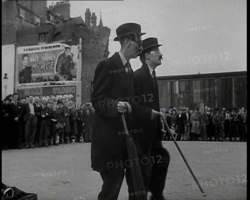 Two British Men in Suits and Hats Dancing in a Square With Men and Woman Watching Them..., 1938. Creator: British Pathe Ltd.