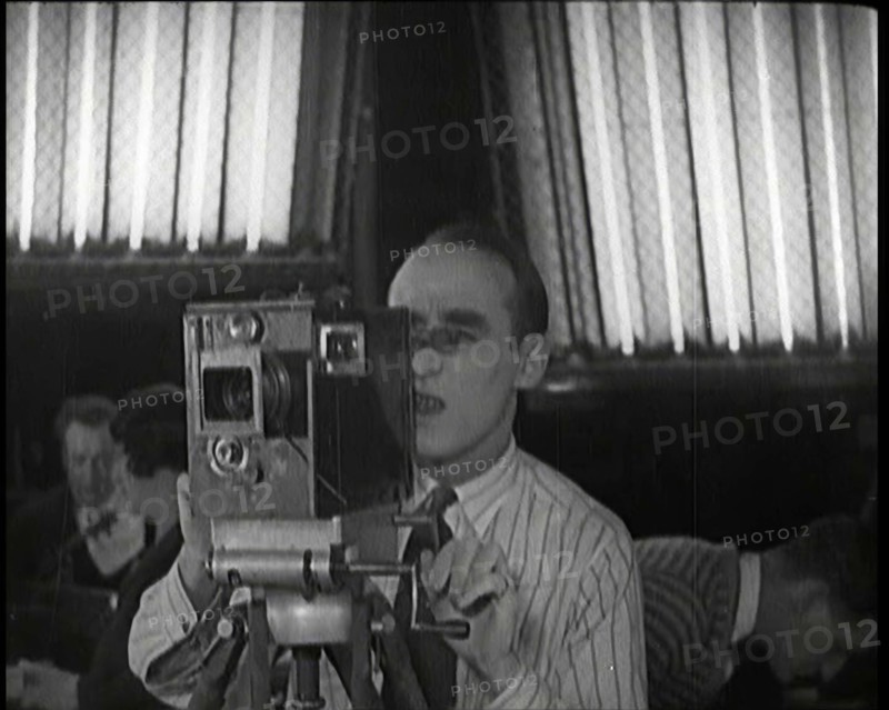 A Male Cameraman Films a Scene Whilst Lights Illuminate Behind Him, 1920s. Creator: British Pathe Ltd.