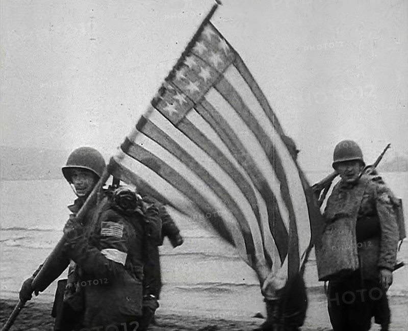 An American Soldier Holding an American Flag on a North African Beach as Part of 'Operation...1942. Creator: British Pathe Ltd.