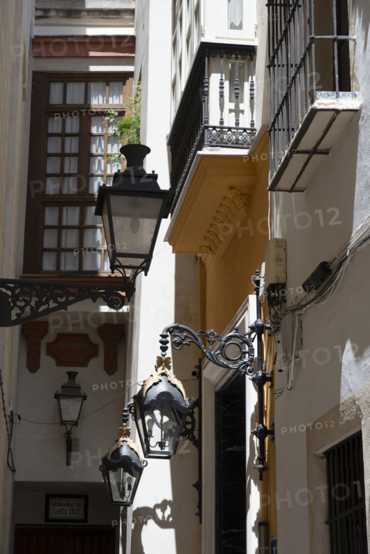 Narrow street with old lamps and balconies in the pedestrian area of Seville, Spain, 2023. Creator: Ethel Davies.