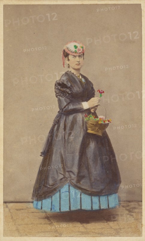 Unidentified woman wearing a flowered hat, holding single flower in one hand, basket of...1862-1865. Creator: Carlo Ponti.