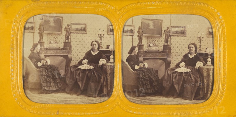 Two women seated in a parlor, one is sewing, the other with a hand fan in her lap, 1860s. Creator: E Lamy.