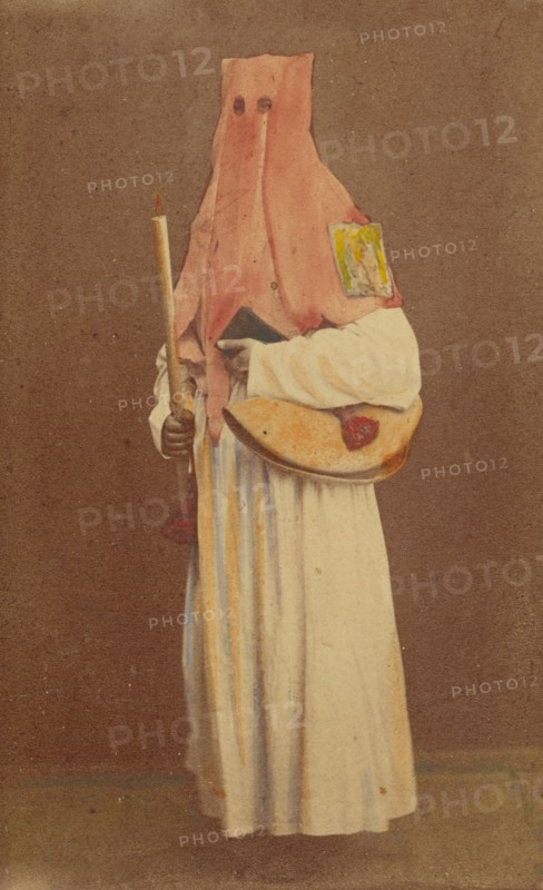 Unidentified man in long hood holding a candle and book, standing, about 1870. Creator: Giorgio Conrad.