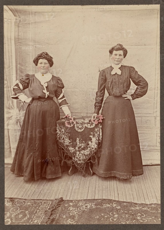 Two women standing at a table holding flowers, about 1875. Creator: Unknown.