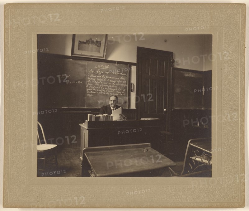 Portrait of a male mathematics teacher with moustache seated at his classroom desk, about 1900. Creator: Unknown.