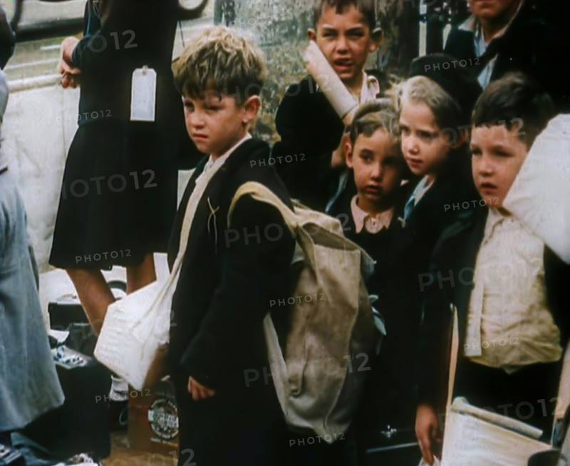 British Child Evacuees Standing on a Pavement With Bags and Boxes as Adults are Standing..., 1939. Creator: British Pathe Ltd.
