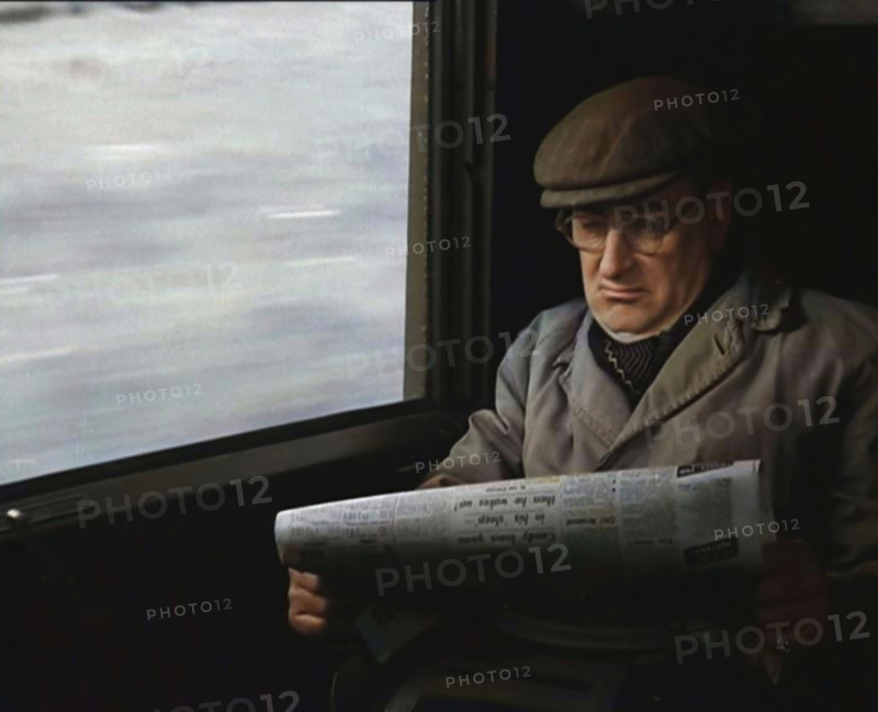 A Man in a Flat Cap and Spectacles Reading a Folded Newspaper in the Window Seat of a Train..., 1938 Creator: British Pathe Ltd.
