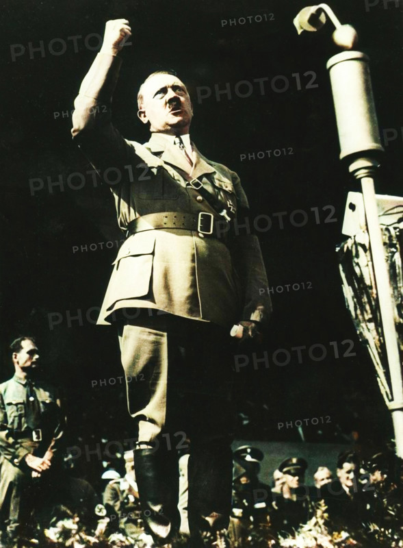 Adolf Hitler addressing a Nazi rally at Nuremberg, Germany, 1930s. The Nazi Party held annual political rallies at Nuremberg from 1927 until 1938. After the Nazis claimed power in 1933 the rallies became massive state propaganda events. Hitler's deputy, Rudolf Hess, is in the bottom left of the picture. (Colorised black and white print).