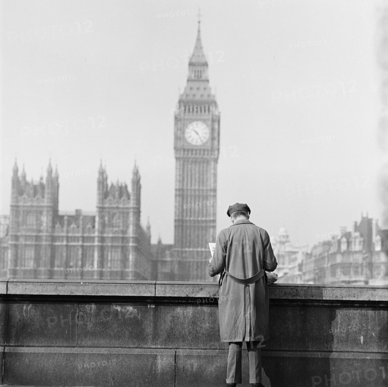 Houses of Parliament seen from the Albert Embankment with a man reading a newspaper by the parapet in the foreground, London, 1964.