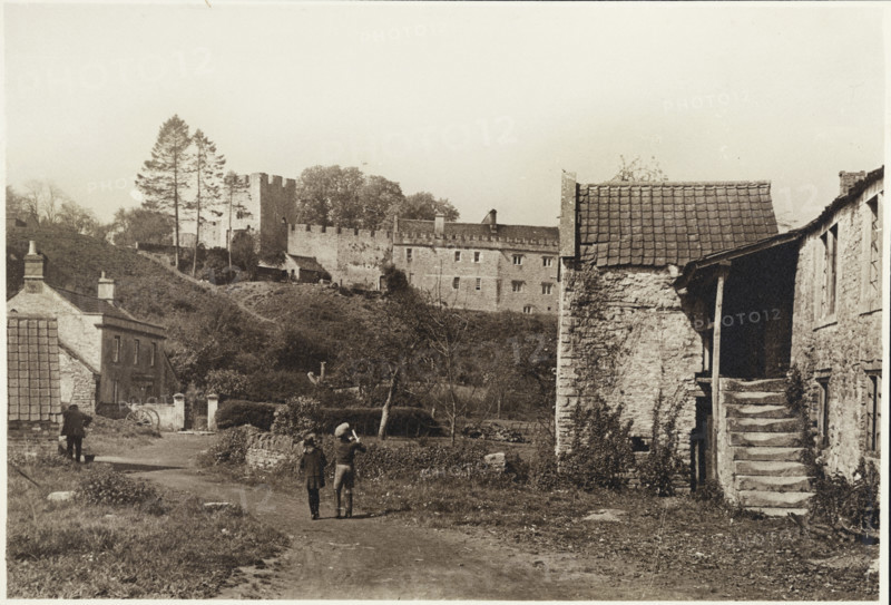 General view of Farleigh Hungerford Castle from the east, Norton St Philip, Mendip, Somerset, 1920-1950; with children in the foreground walking past two village houses below the castle.