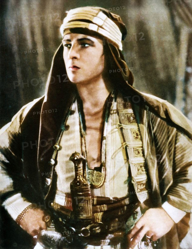 Rudolph Valentino in "The Sheik", 1921, (1935). Portrait of Rudolph Valentino (1895-1926), film actor born in Italy, one of the first 'Hollywood heartthrobs'. Valentino arrived in the United States in 1913 and found fame as a film star and sex symbol of the 1920s. When he died at the age of 31, of complications after surgery for appendicitis and gastric ulcers, 100,000 people lined the streets of Manhattan in New York to pay their respects at his funeral. From "The Silver Jubilee Book - The Story of 25 Eventful Years in Pictures". [Odhams Press Ltd., London, 1935], (Colorised black and white print).