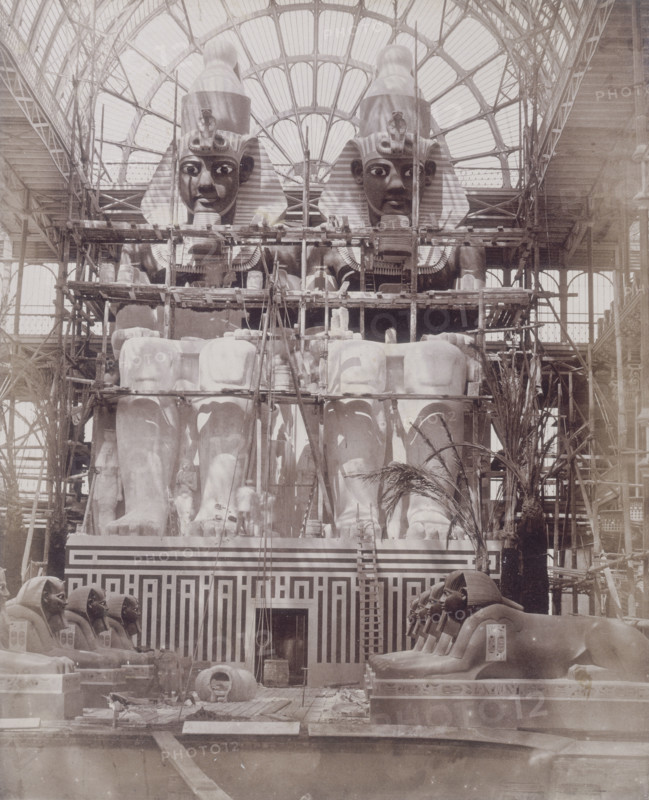 'The Colossi of Aboo Simbel in Process of Painting', Crystal Palace, Sydenham, 1852-1854. Designed by Sir Joseph Paxton to house the Great Exhibition of 1851 in Hyde Park, the Crystal Palace was reconstructed and enlarged in Sydenham in 1852. The first column was raised on 5 August 1852 and the palace was opened by Queen Victoria on 10 June 1854. Many exhibitions and events were subsequently held at the Crystal Palace until it burnt down on 30 November 1936. The park contained a motor racing circuit from 1937 until 1972 and the famous athletics track dates back to the foundation of the Crystal Palace Athletics Club in 1868. Plate 64 from "Photographic Views of the Progress of the Crystal Palace, Sydenham. Taken during the progress of the works, by desire of the directors, by Philip H Delamotte. Together with a list of the directors and officers of the company, etc". [London, 1855].