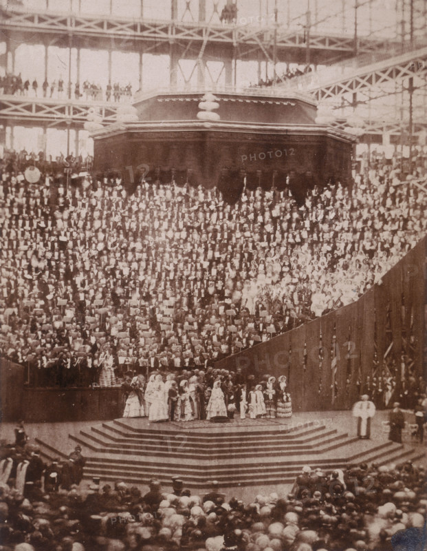 'The Opening Ceremony', Crystal Palace, Sydenham, 1852-1854. Designed by Sir Joseph Paxton to house the Great Exhibition of 1851 in Hyde Park, the Crystal Palace was reconstructed and enlarged in Sydenham in 1852. The first column was raised on 5 August 1852 and the palace was opened by Queen Victoria on 10 June 1854. Many exhibitions and events were subsequently held at the Crystal Palace until it burnt down on 30 November 1936. The park contained a motor racing circuit from 1937 until 1972 and the famous athletics track dates back to the foundation of the Crystal Palace Athletics Club in 1868. Plate 99 from "Photographic Views of the Progress of the Crystal Palace, Sydenham. Taken during the progress of the works, by desire of the directors, by Philip H Delamotte. Together with a list of the directors and officers of the company, etc". [London, 1855].