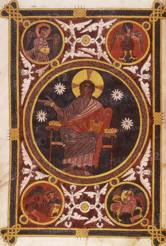 Christ in majesty, 1109. Set within a circle, his right hand raised in blessing, and holding a book in his left hand. In the background are four stars. With stylised floral borders and Celtic knot patterns. In the corners are four roundels with the symbols of the evangelists: angel, eagle, bull and lion. Around these are pairs of coiled serpents and human heads with foliate motifs emerging from their mouths. From the Silos Apocalypse.