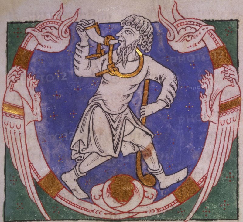 Amos, 1148. Beginning of the Book of Amos. Initial 'V', Amos blowing a horn, and carrying a club, between two winged creatures with entwined tails. From the Parc Abbey Bible.