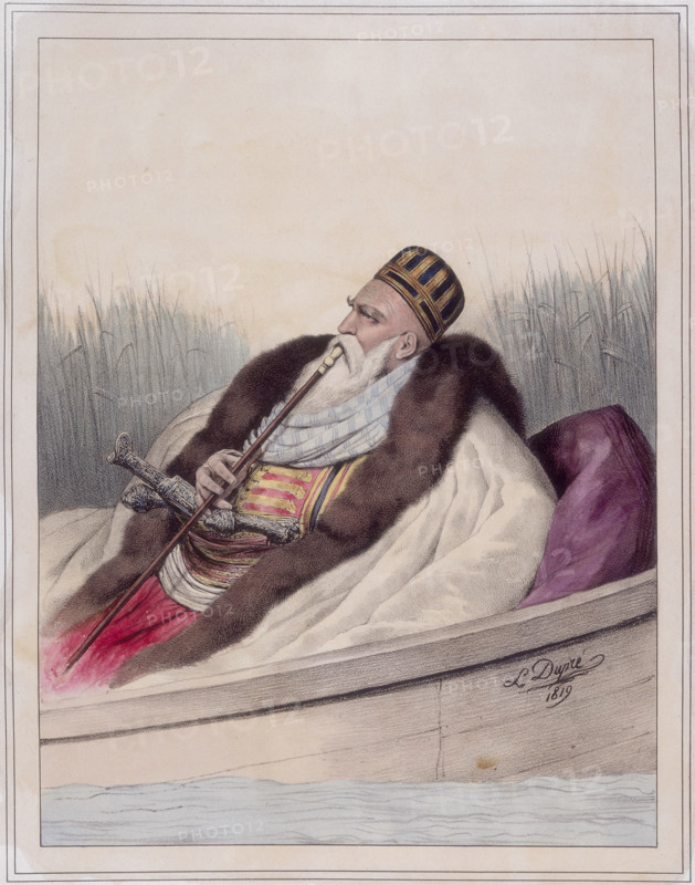 Ali Tebelen, Pacha de Janina, 1819. Ali Pasha (1741-1822) reclining in a boat smoking a pipe, and wearing a coat trimmed with fur. In 1787 he became the Turkish pasha (military governor) of Yannina, which is now Ioánnina in Greece, but was a province of the Ottoman Empire. He was called the lion of Yannina because of his harsh rule. From "Voyage à Athènes et à constantinople; ou collection de portraits, vues et costumes Grecs et Ottomans".