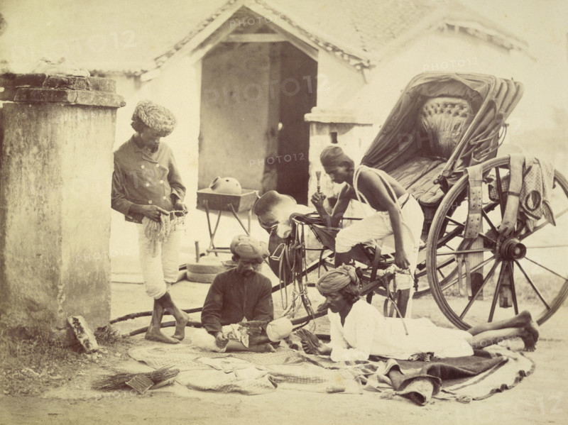Four men and a rickshaw, India, 1873. Two are playing cards. The man on the right holds a chillum, and the man on the left may be cleaning a horse's bit.