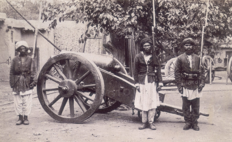 Three Afghan soldiers standing next to a cannon, Afghanistan, 1880s. Their rifles have bayonets fitted to them. Compared to the British Army their uniforms are very basic; military jackets over their normal clothes.