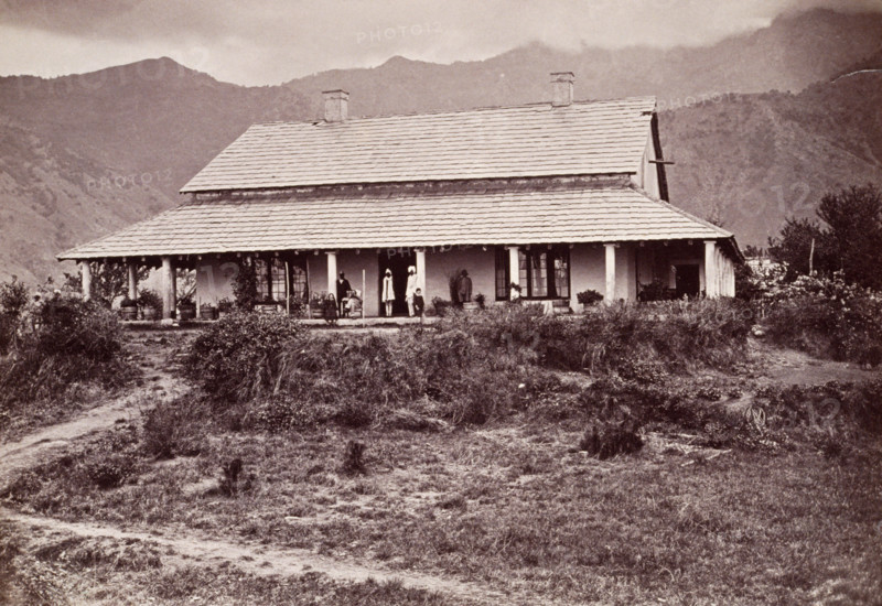 Tea estate bungalow at Sumali, 1860s. European man and children on the verandah, with Indian servants.