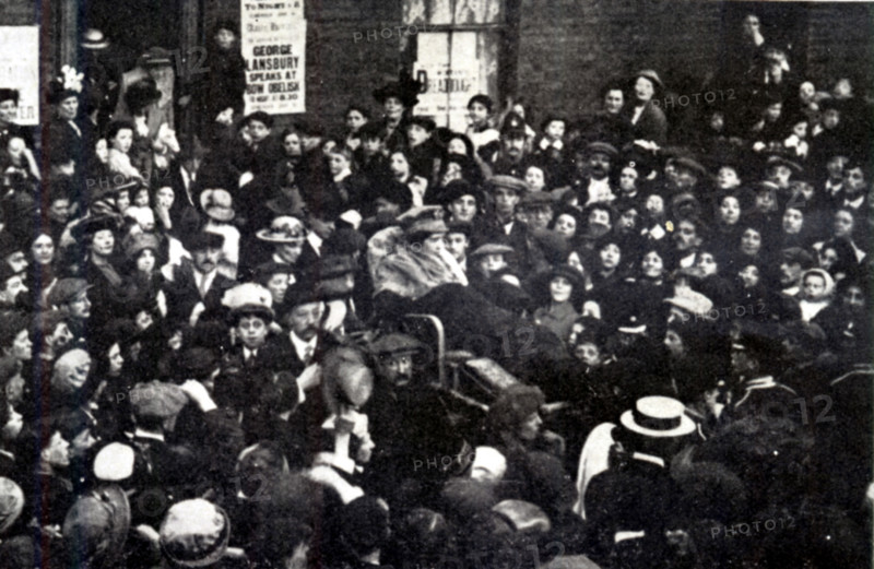 East London sets forth to interview the Prime Minister, HH Asquith, at the House of Commons, carrying Sylvia Pankhurst, London, June 10, 1914. British feminist, socialist activist and writer Sylvia Pankhurst (1882-1960) on hunger strike, carried by supporters during women's fight for the vote. A poster reads: 'George Lansbury speaks at Bow Obelisk'. From Pankhurst's "The Suffragette Movement. An intimate account of persons and ideals". [1931].