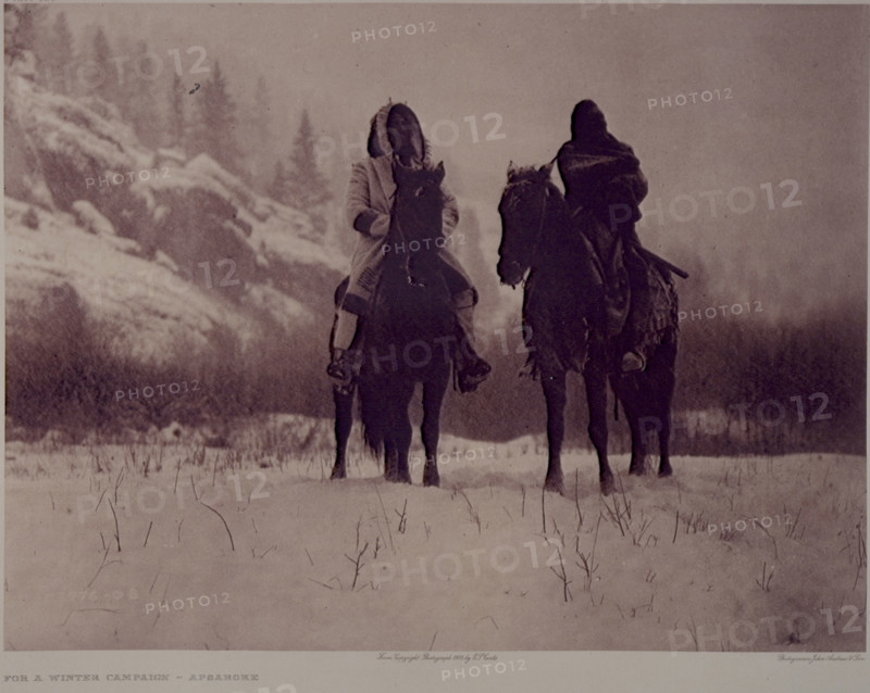 'For a Winter Campaign - Apsaroke', 1909. North American Indians on horseback. The warrior on the left wears the hooded overcoat of heavy blanket material that was generally adopted by the Apsaroke after the arrival of traders among them. The photograph was taken in a narrow valley among the Pryor mountains, Montana. From "The North American Indian: The complete Portfolios" by Edward S Curtis. [1909].