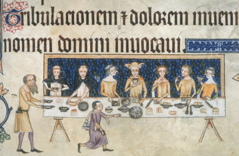 Sir Geoffrey Luttrell dining with his family, c1325-c1335. Sir Geoffrey Luttrell is seated in the centre of a long table supported on two trestles, behind is a blue hanging with the Luttrell martlets in silver. On his left, his wife, Agnes Sutton, and two Dominicans, perhaps his chaplain, Robert of Wilford, and his confessor, William of Foderingeye. On Luttrell's right, two men and a lady. A bearded servant brings two dishes, and a cup-bearer kneels, having given his cup to Sir Geoffrey. On the table are knives, spoons, dishes, and plates or trenchers of bread . From the Luttrell Psalter.