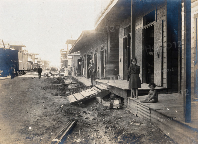 Colón, Panama: unpaved street lined with wooden houses; two children watch from a porch..., 1906. Creator: Unknown.