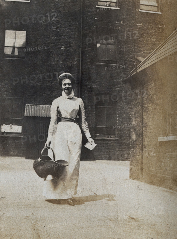 St Bartholomew's Hospital, London: a smiling nurse carrying a coal scuttle, c1890. Creator: Unknown.