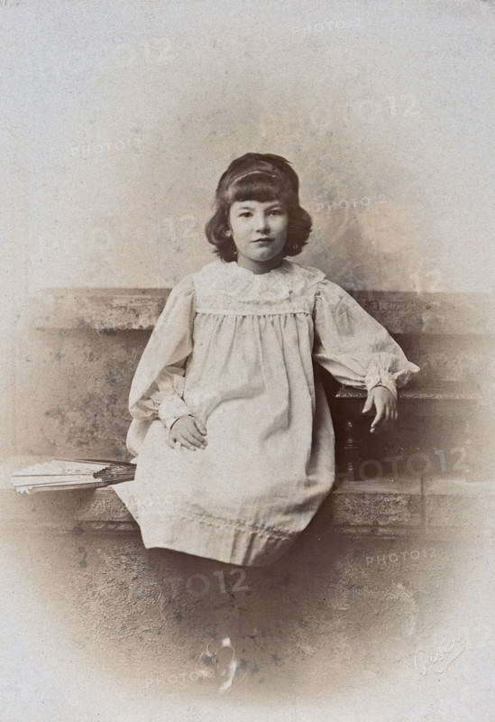 A girl, sitting on a stone bench with a fan folded at her side, c1890s. Creator: Arthur Reston.
