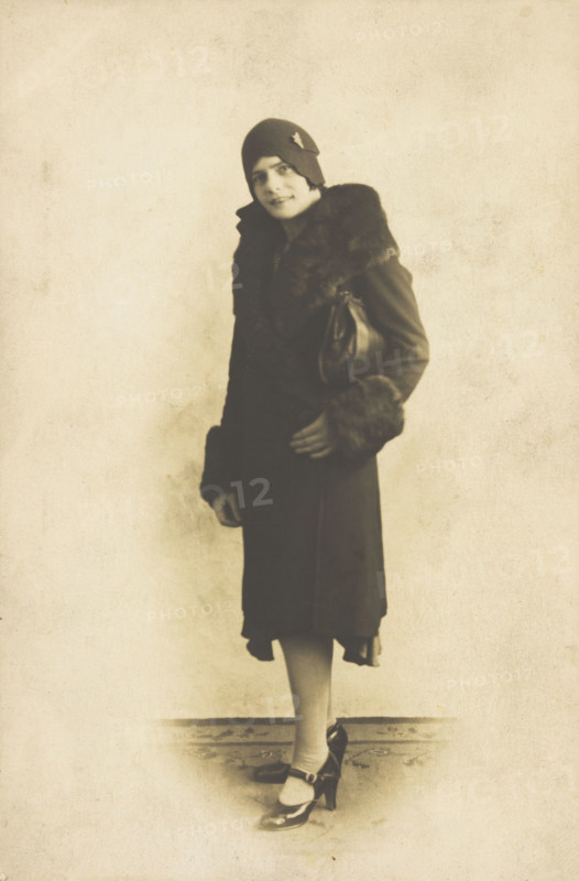 A person poses wearing a long coat with fur trim and a hat with a brooch, [between 1920 and 1929?]. Creator: Unknown.