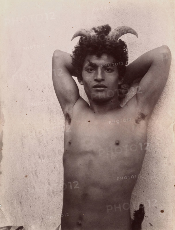 A Sicilian boy naked from the waist up, his hands behind his head, wearing horns, 3 Feb 1899. Creator: Count Wilhelm von Gloeden.