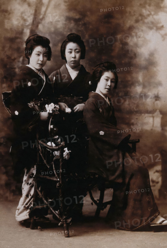 Three young women posing in a photographic studio, one seated on a bench..., early 20th century. Creator: Unknown.