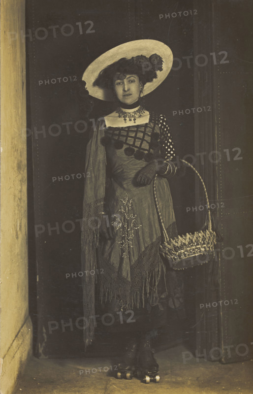 A person wearing a dress, large hat and roller skates, poses holding a basket, (1910-1919?). Creator: Unknown.