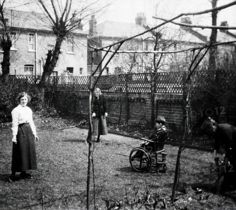 A physically disabled boy sitting in a wheelchair in the back garden of a semi..., c1910/1925. Creator: Unknown.