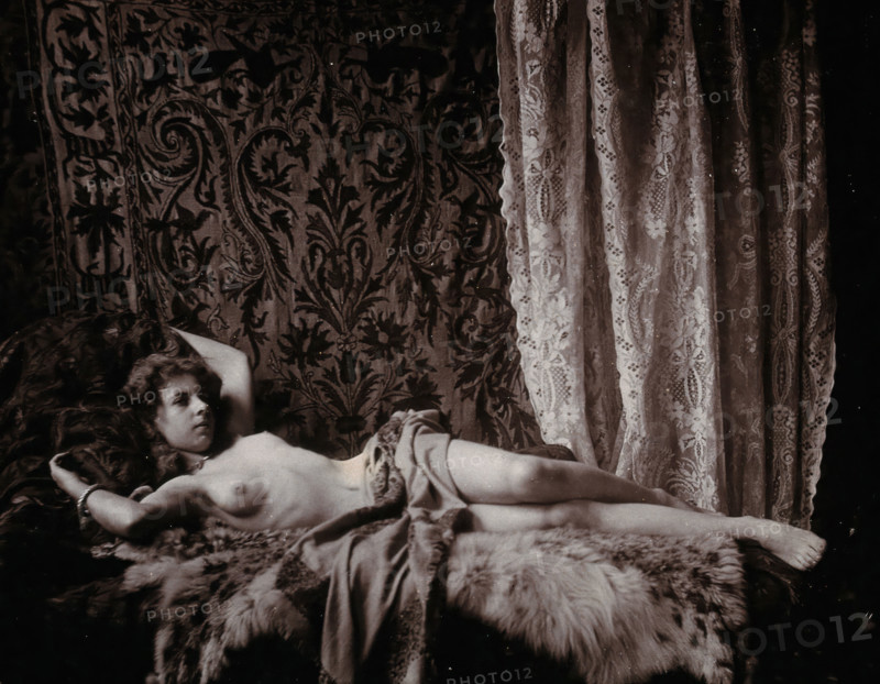 A young woman, posing semi-naked in a photographic studio, lying full-length on a fur..., c1900. Creator: Unknown.