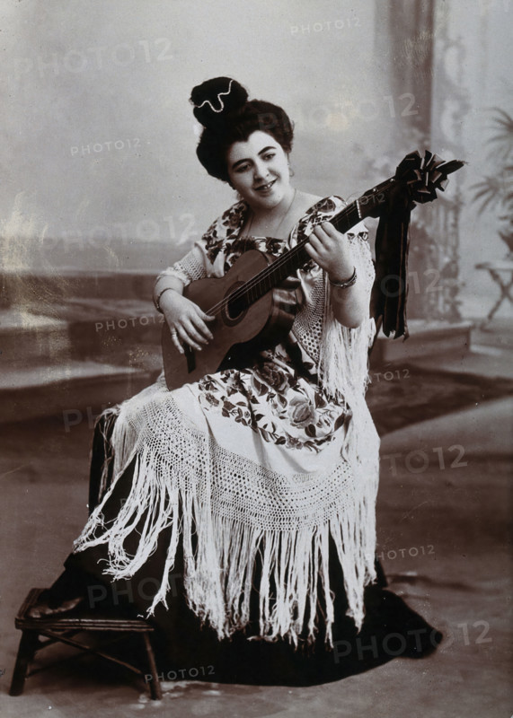 A seated woman, playing a guitar, wearing a fringed shawl, c1900. Creator: Unknown.