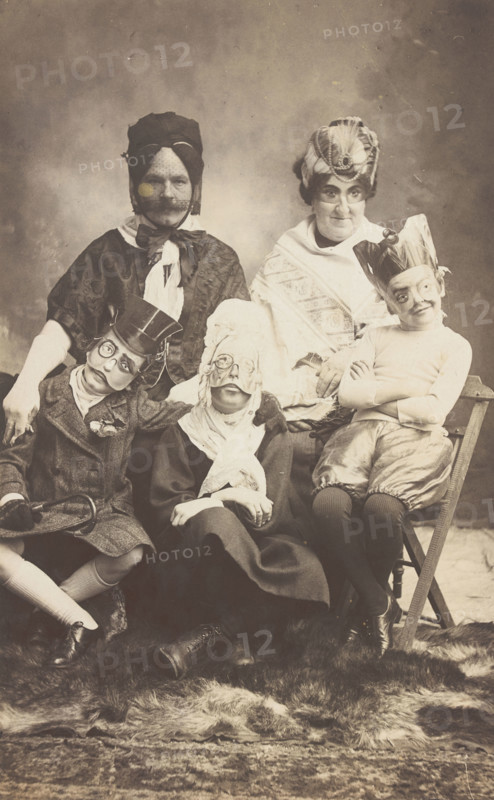 A family, all members wearing grotesque masks, the father in drag, c1910. Creator: Unknown.