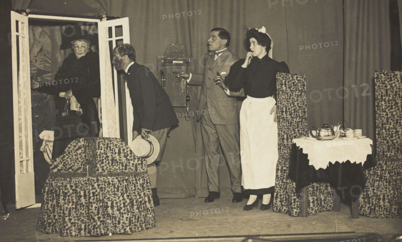 Amateur actors, one in drag, perform a scene on stage, [between 1910 and 1919?]. Creator: Unknown.