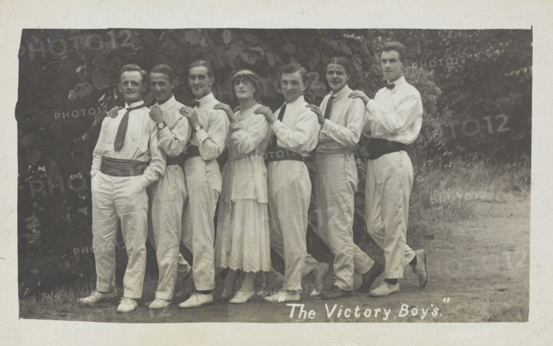 Entertainers, one in drag, pose in a line in front of foliage, [between 1910 and 1919?]. Creator: Unknown.