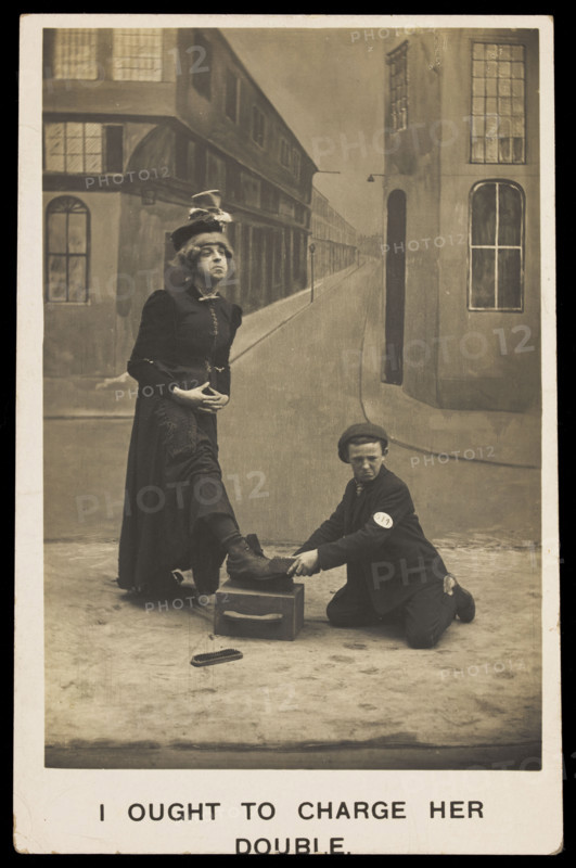 A shoeshine boy cleans the boots of a man in drag, c1905. Creator: Unknown.
