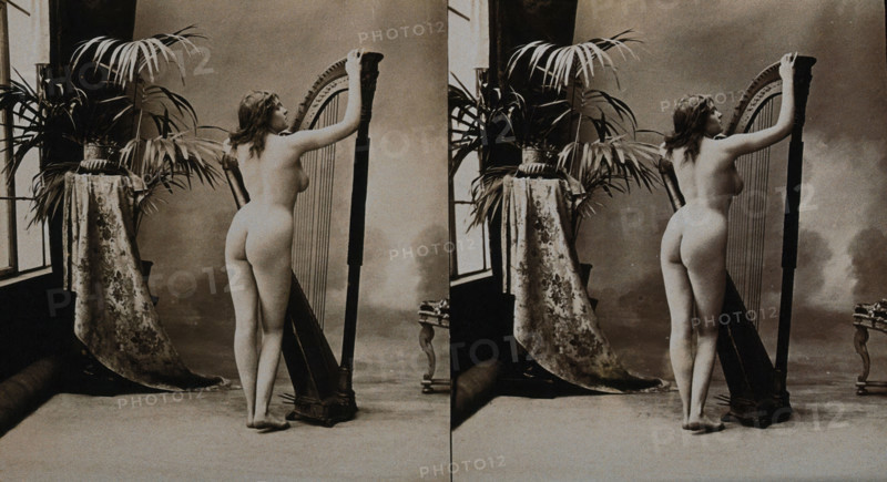 A young woman posing naked in a photographic studio, standing with her back to the camera..., c1900. Creator: Unknown.