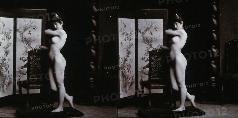 A young woman posing naked in a photographic studio, leaning on the back of a chair..., c1900. Creator: Unknown.