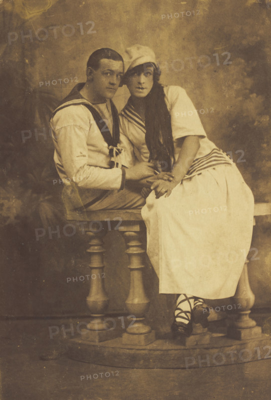 Two sailors, one in drag, embracing while sitting on a stage balcony, (between 1910 and 1919?). Creator: Unknown.