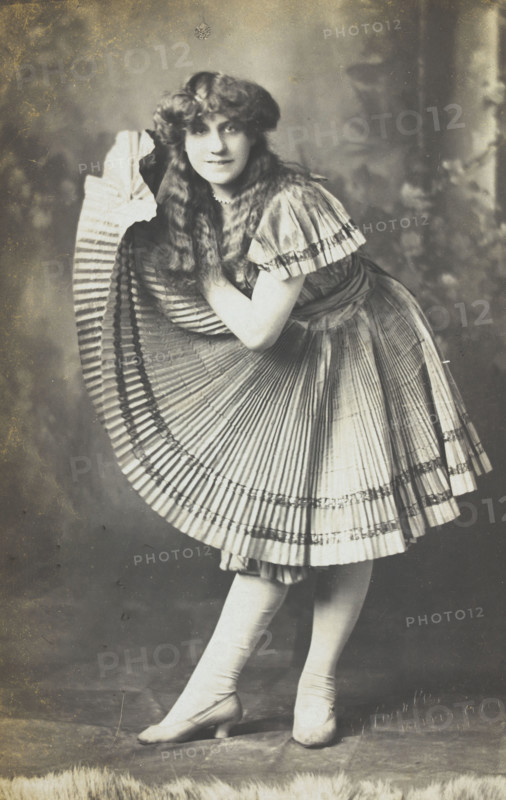 An amateur actor in drag holds up his impressive folded dress to one side, (between 1910 and 1919?). Creator: Unknown.