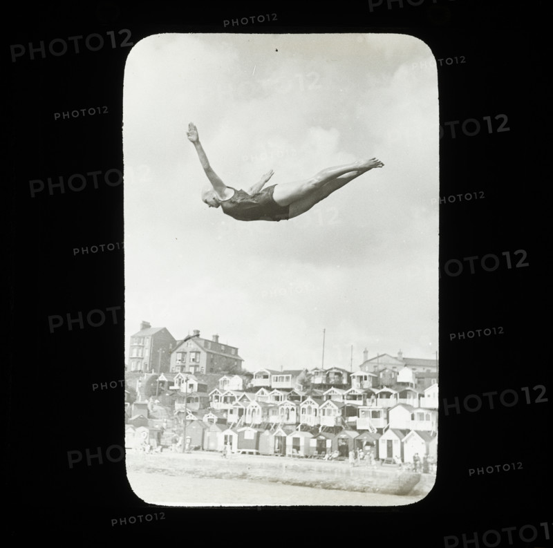 A swimmer diving into the sea at Southcliff, Walton-on-the-Naze, with beach huts on South..., 1920s. Creator: Norman Kingsley Harrison.