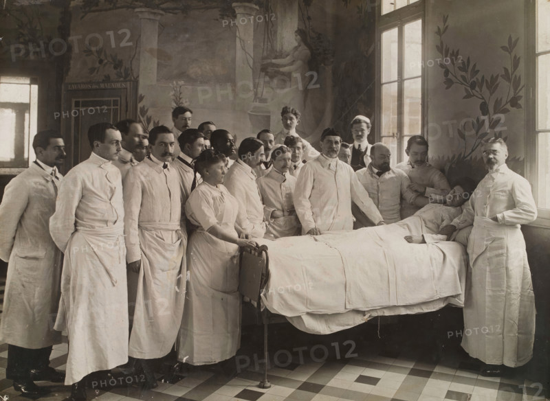 Medical staff standing round a woman patient in bed in a hospital ward, c1910. Creator: Freres Seeberger.