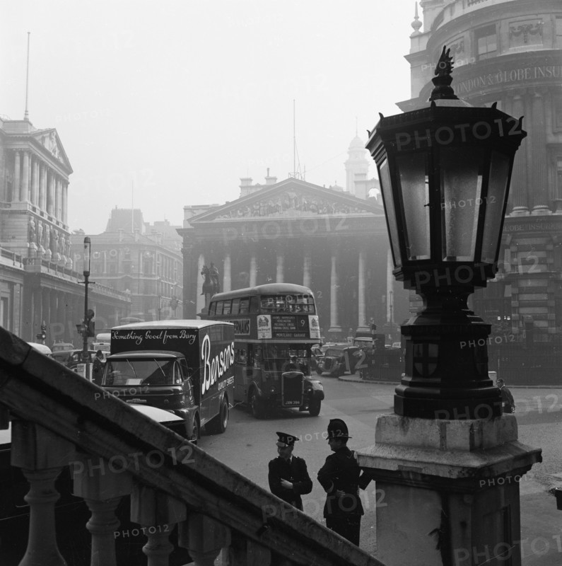 View past a lamp showing the busy traffic outside The Bank of England..., London, probably 1960s. Creator: John Gay.