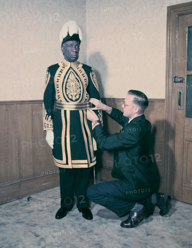 A Paramount Chief being fitted for his robes for the coronation of Queen Elizabeth II, 1953. Creator: Arthur Charles Kirby Ware.