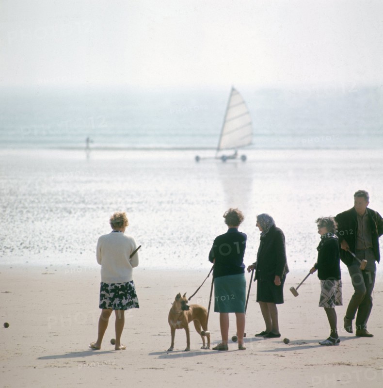 Dans les années 1970, sur une plage normande, des vacanciers jouent au croquet en regardant passer les chars à voile.